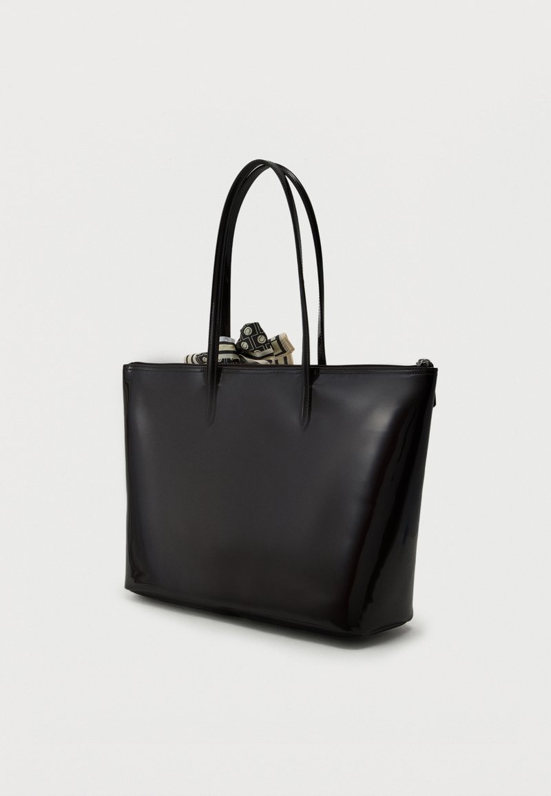 Black shiny tote bag with two thin handles, partly open top showing a black and white patterned scarf inside, against a plain light background.