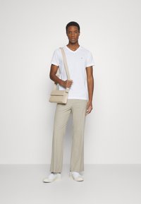 T-shirt blanc à col en V, sac bandoulière beige, et pantalon en plaid beige à coupe décontractée, associés à des baskets blanches sur un fond neutre.