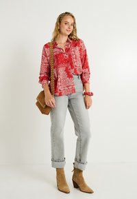 Chemise à motifs paisley rouges avec manches longues, jeans droits gris clair, bottines chelsea en daim marron et sac bandoulière marron.