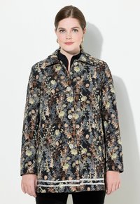 Mustaa kukkakuosiset takki, jossa on vihreän, persikan ja kullan sävyjä. Napitus, kaulus ja teksturoitu kangas korostuksilla.