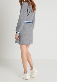 Robe sweat grise à manches longues, avec une taille rayée en bleu, noir et blanc. Portée avec des baskets blanches.