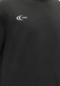 Μαύρο μπλουζάκι με στρογγυλή λαιμόκοψη, με μικρό λευκό λογότυπο "ARKK" και καμπύλο σχέδιο στο αριστερό στήθος.