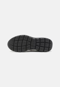 Black rubber shoe sole featuring a textured surface with defined tread patterns and multiple rectangular lugs for traction.