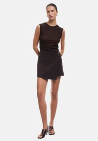 Top negro sin mangas combinado con una falda cruzada oscura, que presenta un bolsillo lateral y un detalle de metal dorado. El conjunto se completa con unos tacones destalonados.