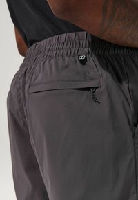 Graue Sportshorts aus leichtem Stoff mit einem elastischen Bund, einer seitlichen Reißverschlusstasche und einem kleinen Logo-Detail auf der Rückseite.