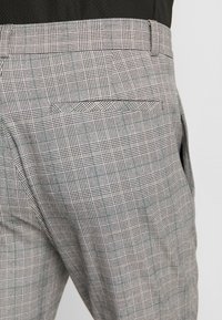 Pantalon gris à carreaux avec un motif pied-de-poule et des accents verts, doté d'une poche arrière et d'une texture de tissu douce et structurée.