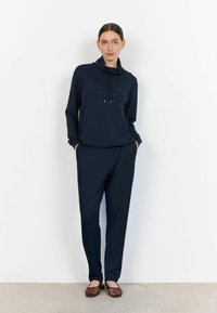 Marineblauer Hoodie mit Kapuze und Kordelzügen, bedruckt mit dem Text "Lasst neue Abenteuer beginnen", kombiniert mit passenden lockeren Hosen und braunen Schuhen.