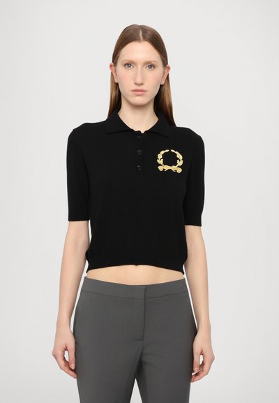 Polo noir court avec des manches courtes, arborant un logo de couronne de laurier brodé en or, une patte de boutonnage et une texture en maille douce.