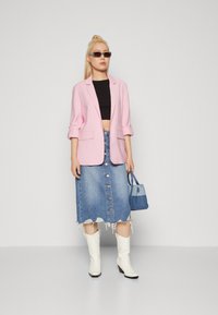 Roze sako, crni crop top, plava traper suknja s dugmadi, bijele kaubojke i mala plava torba. Glatka tkanina, opušteni kroj, izgužvan rub.