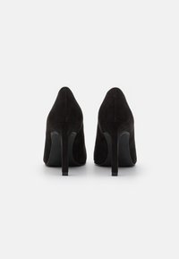 Ein Paar schwarze Wildleder-Pumps von hinten auf einem weißen Hintergrund abgebildet.