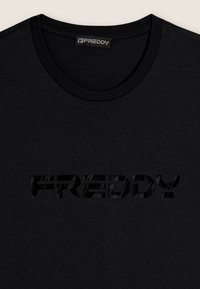 Camiseta de algodón negra con cuello redondo y un logo texturizado tonal "FREDDY" impreso en el frente. Tejido suave y diseño sencillo.