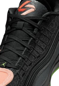 Scarpa sportiva nera con tessuto strutturato, dettagli rosa e logo verde. Le stringhe sono prominenti, con un dettaglio di design elegante e curvo.