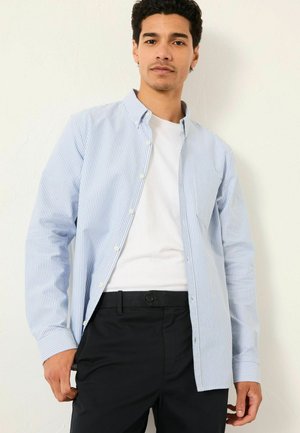 Hellblau-weiß gestreiftes Button-Up-Hemd mit langen Ärmeln, kombiniert mit schwarzen Hosen. Das Hemd hat einen Kragen und eine Fronttasche.