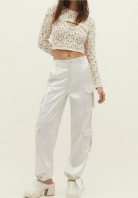 Witte, satijnen cargo broek met zijzakken en elastische boorden, gecombineerd met een cropped, gebreide trui met een gestructureerd, open patroon.