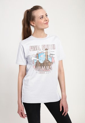 Ung kvinde med langt hestehale iført en hvid Pink Floyd Animals Tour ’77 T-shirt og sorte bukser, ser op mod venstre.