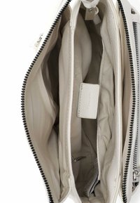 Wnętrze białej skórzanej torebki z trzema przegrodami, beżową podszewką materiałową, zamkiem błyskawicznym oraz małą skórzaną metką. Gładkie i fakturowane powierzchnie.