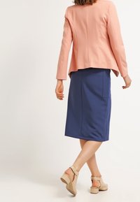 Růžový blejzr s pevnými rameny, který je spárován s sukní střední délky v námořnické modři. K outfitu dokonale ladí béžové sandály na kotníku.