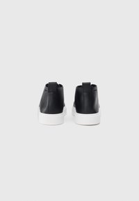 Adidași negri din piele cu un design înalt, tălpi de cauciuc alb, și curele de tragere la spate; branding minimal vizibil pe laturi.