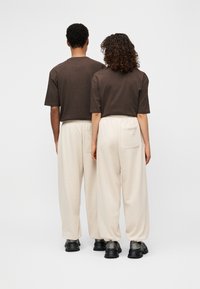 Καφέ κοντά μπλουζάκια σε συνδυασμό με μπεζ φόρμες, με ελαστικές μέσες και δύο πίσω τσέπες. Μαύρα αθλητικά παπούτσια ολοκληρώνουν την εμφάνιση.