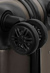 Gros plan sur deux roues noires à rotule attachées à une valise rigide marron texturée près de sa couture de fermeture éclair.
