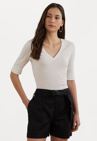 Top bianco a V, aderente, con tessuto texturizzato e maniche a tre quarti, abbinato a pantaloni shorts neri larghi con cintura annodata e tasche.