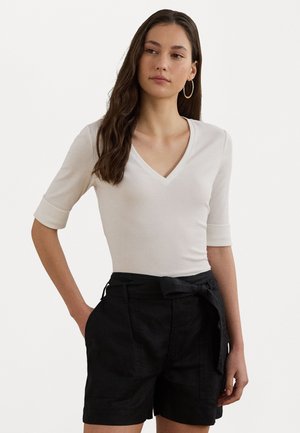 Un haut blanc ajusté à col en V avec un tissu texturé et des manches 3/4, associé à un short noir ample avec une taille ceinturée et des poches.