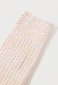 Calzino rigato beige chiaro con finitura testurizzata. Il polsino presenta un motivo di maglia fine, che si trasforma in un corpo liscio con sottili righe.