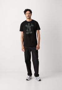 Camiseta de algodón negra con gráfico de Mickey Mouse a cuadros. Combinada con pantalones cargo negros y zapatillas grises. Diseño simple y ajuste relajado.