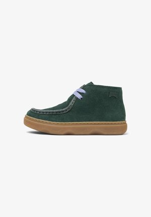 Green suede footwear with a rounded toe, featuring light purple laces and a tan rubber sole, angled to reveal side details.