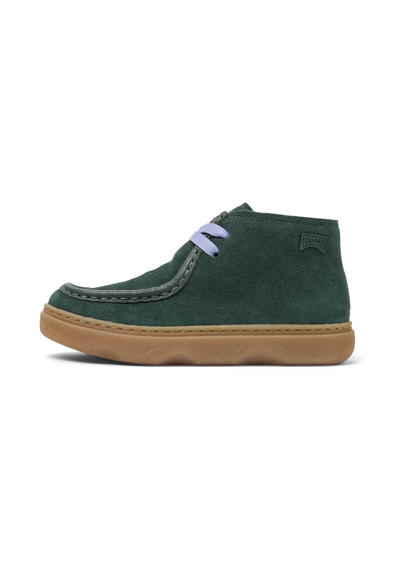 Calzado de ante verde con punta redondeada, que presenta cordones en un tono morado claro y una suela de goma marrón, en un ángulo que revela los detalles laterales.