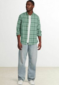 Groen geruite knoopshirt met lange mouwen, een wit T-shirt eronder, losse lichtblauwe jeans en witte sneakers.