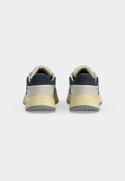 Paire de baskets beige et marine vues de dos avec col rembourré et semelles intermédiaires épaisses beiges sur fond blanc uni.