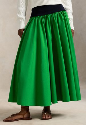 Zelená maxi sukňa so zberaným pásom, čiernym elastickým pásikom a vzdušným strihom. Nosená s hnedými sandálmi so šnúrkami.