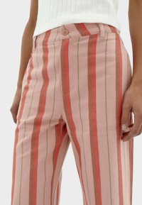 Gestreepte roze broek met verticale strepen in rood en groen, gemaakt van een gestructureerde stof met een knoopsluiting en zijzakken.