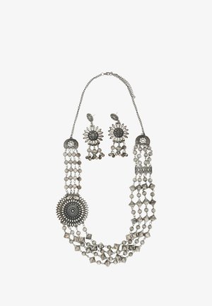 Colier argintiu cu șiruri de mărgele în straturi, medalion central ornamentat și cercei asortați cu model florar, care prezintă detalii intricate.