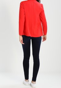 Punainen bleiseri pitkillä hihoilla, istuva malli, sileä pinta. Yhdistetty tummiin slim fit -farkkuihin ja vaaleisiin tennareihin.