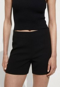 Shorts noirs sur mesure en tissu lisse, présentant un design épuré avec une forme structurée et sans attaches visibles ni motifs.