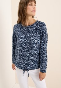 Blusa navy con un motivo astratto azzurro, caratterizzata da un colletto rotondo e un orlo con coulisse. Realizzata in un tessuto leggero.