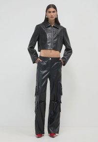 Schwarze, cropped Lederjacke mit Kragen und Frontreißverschluss, kombiniert mit hochgeschnittenen, schwarzen Leder-Cargo-Hosen mit Seitentaschen und Reißverschlüssen.