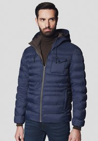 Granatowa kurtka puchowa z poziomym pikowaniem, z kapturem, zamkiem z przodu oraz kieszenią na klatce piersiowej, noszona z brązowym golfem pod spodem.