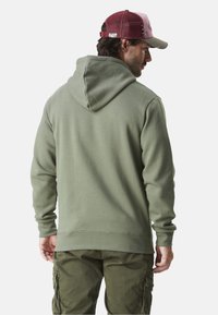 Sweat-shirt à capuche vert avec une finition texturée, présentant des manches longues et une poche kangourou. Associe à un pantalon cargo olive, mettant en avant des détails utilitaires.