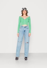 Sweater cropped verde com riscas e design à mostra ombros, combinado com jeans de perna larga desbotados em azul claro e sapatos plataforma pretos com padrão floral.