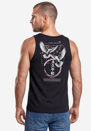 Man wearing black tank top with graphic of two white doves, cherry blossoms, and text including "Inner Peace" on the back.