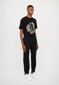Black t-shirt with a colorful graphic design, paired with black tapered sweatpants and white sneakers featuring black accents.