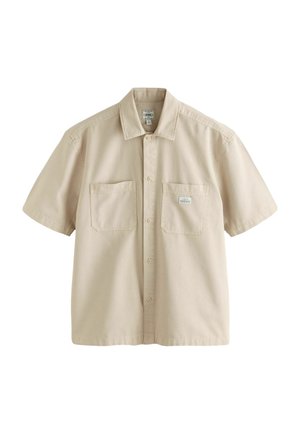 Bež srajca s kratkimi rokavi iz bombaža, ki ima gumbasto zapiranje spredaj, dve prsni žep, in ravno obrobo z diskretnimi šivnimi podrobnostmi.