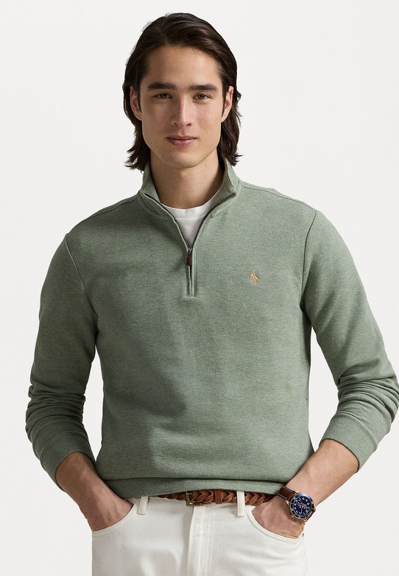 Light green knit pullover with a quarter-zip collar, featuring a small logo and ribbed cuffs. Textured fabric with a casual fit.