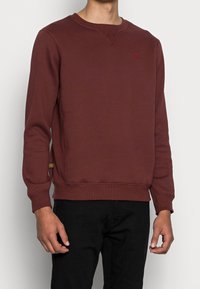 Sudadera burdeos hecha de mezcla de algodón, con cuello y puños acanalados, pequeño logo en el pecho y detalle de etiqueta lateral.