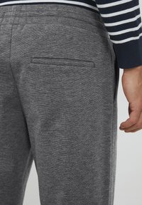 Graue Jogginghosen aus strukturiertem Material, mit einer Gesäßtasche und einem elastischen Bund, kombiniert mit einem gestreiften langärmligen Oberteil in Marineblau und Weiß.