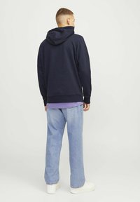 Sudadera con capucha azul marino y bolsillo canguro, combinada con jeans de pierna ancha en azul claro y zapatillas blancas. Textura suave, ajuste casual.