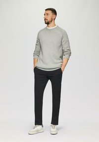 Szary sweter robiony na drutach z prążkowanymi mankietami, zestawiony z czarnymi dopasowanymi spodniami i białymi trampkami z delikatnymi akcentami.